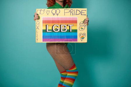 Photo for Crop unrecognizable transgender person in stockings and colorful rainbow socks demonstrating placard with LGBT symbols and pride inscription against blue background - Royalty Free Image