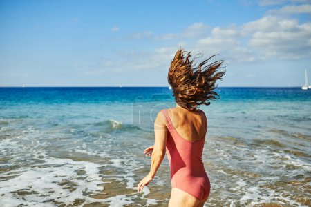Foto de Mujer madura que se divierte saltando en la playa durante las vacaciones de verano - Concéntrate en la espalda femenina - Imagen libre de derechos