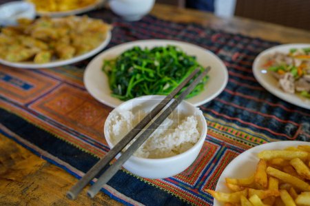Téléchargez les photos : Riz savoureux dans un bol blanc avec des baguettes placées près des algues et des frites contre des rouleaux de printemps vietnamiens sur la table avec de la nourriture orientale traditionnelle - en image libre de droit