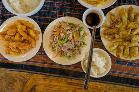 Foto de Vista superior de la ensalada vietnamita con cerdo frito y rodajas de jengibre en el plato cerca de rollos de primavera y arroz contra camarones en masa y salsa de soja servida con palillos en la mesa - Imagen libre de derechos