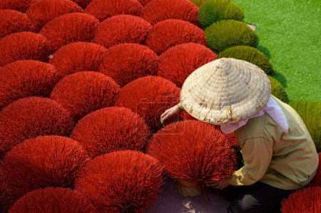 Photo for From above of anonymous Vietnamese vendor in conic hat adjusting bunches of red colored incense sticks - Royalty Free Image