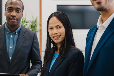 Téléchargez les photos : Satisfait collègues multiraciaux masculins et féminins en vêtements formels regardant la caméra tout en se tenant debout dans le bureau moderne - en image libre de droit