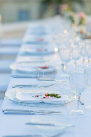 Téléchargez les photos : Verres à vin transparents et assiettes blanches avec argenterie placées sur la table de banquet avec serviette et décorées par des herbes pendant la fête de célébration - en image libre de droit