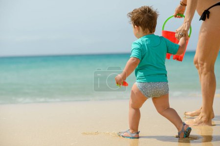 Foto de Vista trasera de un niño pequeño con ropa casual jugando con juguetes en la playa de arena - Imagen libre de derechos