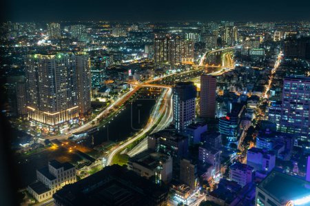 Téléchargez les photos : Vue aérienne de la ville contemporaine colorée avec des gratte-ciel et des immeubles d'appartements résidentiels modernes avec des autoroutes dans des lumières incandescentes la nuit - en image libre de droit