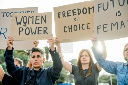 Téléchargez les photos : Rassemblement des féministes en vêtements décontractés lever des pancartes tout en exigeant des femmes à droite avec les bras levés debout à l'extérieur dans le parc - en image libre de droit