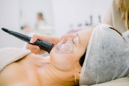 Téléchargez les photos : Cosmétologue anonyme utilisant le massage pour sur le menton du client féminin pendant la procédure de soins de la peau dans le salon de beauté - en image libre de droit