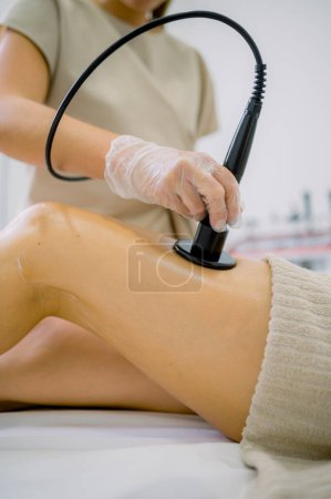 Photo for Anonymous female cosmetologist using massage machine on leg of woman during anti cellulite therapy in beauty salon - Royalty Free Image