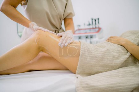 Photo for Anonymous massage therapist in gloves smearing lotion on leg of female client during work in cosmetology clinic - Royalty Free Image