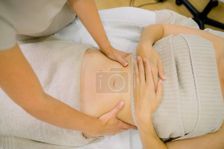 Photo for Top view of unrecognizable massage therapist kneading belly of female client during work in cosmetology clinic - Royalty Free Image