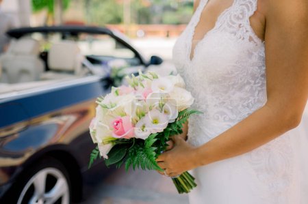 Photo for Unrecognizable woman in white dress with bouquet standing on sunlit street near vehicle during wedding celebration - Royalty Free Image