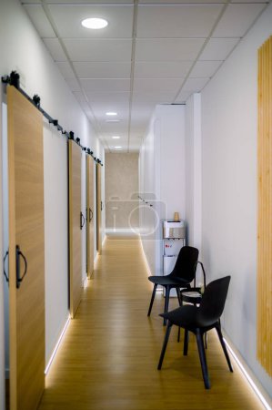 Foto de Vista panorámica del amplio pasillo con puerta de madera y suelo y zona de espera con sillas en la clínica contemporánea - Imagen libre de derechos