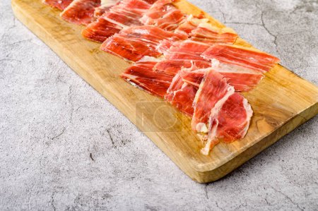 Photo for From above view of thin slices of delicious jamon served on wooden chopping board placed on gray surface - Royalty Free Image