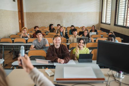 Téléchargez les photos : Groupe de camarades de classe multiethniques souriant et écoutant l'enseignant expliquer la matière pendant la conférence en classe de l'université moderne - en image libre de droit