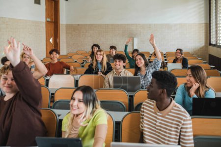 Téléchargez les photos : Adolescents heureux levant les bras et souriant tout en étant assis dans l'auditorium parmi divers camarades de classe pendant la conférence à l'université - en image libre de droit