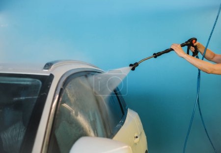 Photo for Unrecognizable female client spraying water on windows of modern vehicle with jet hose against blue wall in self service car wash facility - Royalty Free Image
