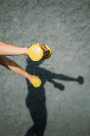 Foto de Alto ángulo de cultivo atleta femenina en mancuernas de elevación de ropa deportiva durante el entrenamiento en el gimnasio - Imagen libre de derechos