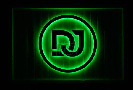 Foto de Letrero creativo DJ en círculo iluminado con luces de neón verde brillante colgando en la pared negra - Imagen libre de derechos