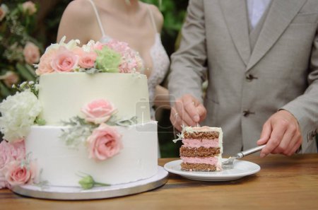 Foto de Cultivo anónimo pareja en vestido de novia de pie en la mesa con delicioso pastel decorado con flores - Imagen libre de derechos