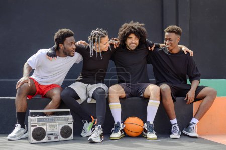 Téléchargez les photos : Groupe d'hommes et de femmes multiethniques en vêtements de sport assis sur le terrain de basket-ball et se regardant - en image libre de droit