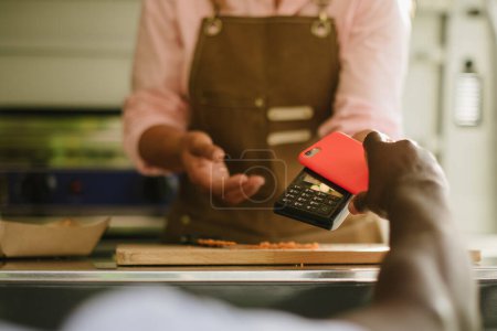 Photo for Soft focus of anonymous African American male using smartphone to pay for order to cook working in food truck - Royalty Free Image