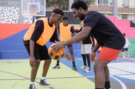 Téléchargez les photos : Vue latérale d'un joueur afro-américain de basket-ball avec une balle debout sur un terrain de sport et se regardant - en image libre de droit