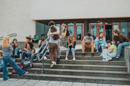 Téléchargez les photos : Groupe d'adolescents divers se reposant sur des escaliers à l'extérieur du bâtiment de la bibliothèque pendant la pause dans les études universitaires pendant la journée - en image libre de droit