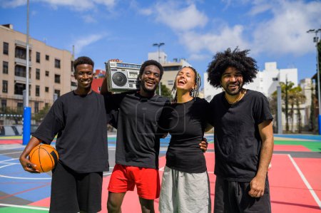 Photo for Delighted African American basketball players in activewear with ball and old fashioned boombox looking at camera while standing on colorful playground and listening to music - Royalty Free Image