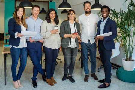 Photo for Group of cheerful multiracial colleagues smiling and looking at camera while standing together during work in modern workplace - Royalty Free Image