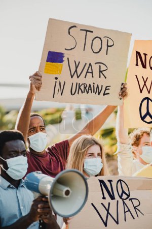 Foto de Jóvenes manifestantes multirraciales protestando contra la guerra de Rusia contra Ucrania con máscaras protectoras al aire libre en la ciudad - Imagen libre de derechos