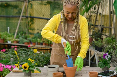 Photo for Happy adult African woman preparing flowers in the nursery garden - Spring green concept - Royalty Free Image