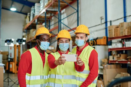 Photo for Happy multiracial workers taking a selfie inside the warehouse safety clothing - Focus on the womans face. - Royalty Free Image