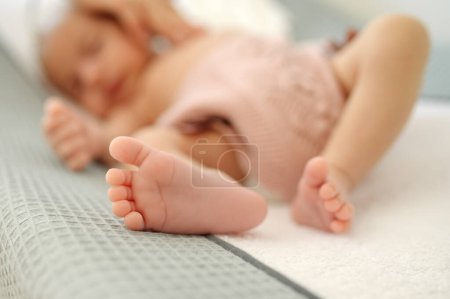 Téléchargez les photos : Adorable bébé flou en vêtements roses avec de jolis petits pieds sur un lit doux à la maison - en image libre de droit