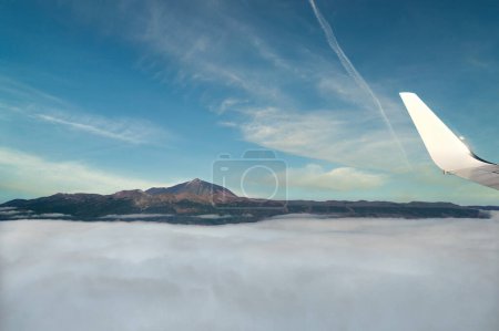 Foto de Pintoresca vista del ala de aviones modernos volando en cielo azul nublado sobre montañas nevadas por encima de una densa nube blanca a gran altitud a la luz del día - Imagen libre de derechos