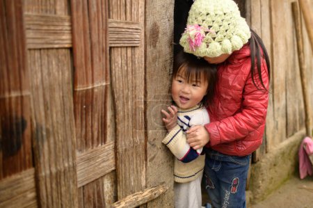 Téléchargez les photos : Petite fille mignonne en vêtements chauds debout près du mur en bois et regardant la caméra - en image libre de droit