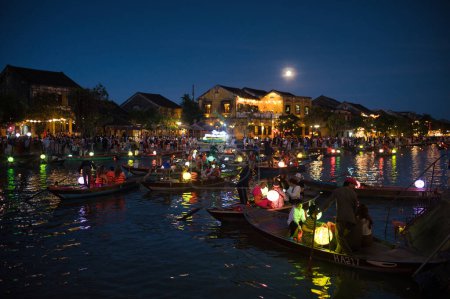 Foto de Personas irreconocibles sentados en barco y flotando en aguas tranquilas de canal por la noche en la ciudad - Imagen libre de derechos