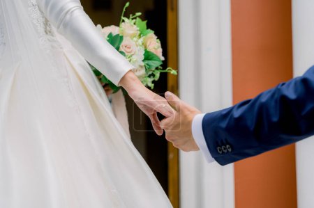 Foto de Novio en traje sosteniendo la mano de las novias con anillo de oro usando vestido de novia blanco sosteniendo ramo durante la boda - Imagen libre de derechos