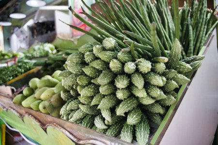 Téléchargez les photos : Divers légumes frais de gourdes amères vertes et de fèves de pilon à la mangue verte placé comptoir de marché sur fond flou - en image libre de droit