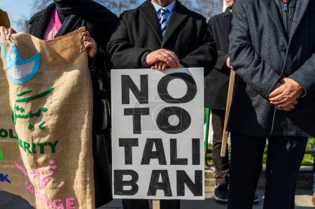 Téléchargez les photos : Manifestants masculins anonymes les mains ensemble dans la rue de Londres et portant une pancarte sans talibans et un sac de jute solidaire en plein soleil - en image libre de droit