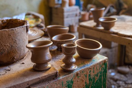 Téléchargez les photos : Pots d'argile placés sur une table minable pour séchage dans un atelier de poterie marocaine sur fond flou - en image libre de droit