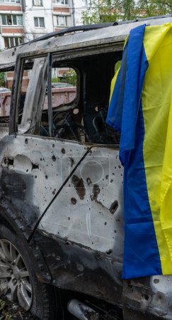 Foto de Bandera de Ucrania en un coche quemado con agujeros de metralla en el lugar de la explosión después del mayor ataque de misiles nocturnos en la capital, el dolor, el concepto de la guerra de Rusia - Imagen libre de derechos