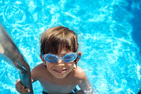 Photo for Boy on the pool ladder with aqua goggles looks at camera - Royalty Free Image