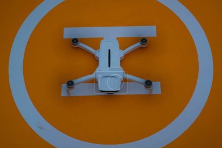 Weiße Drohne bereitet sich auf dem Drohnen-Pad auf den Start vor. Die weiße Drohne steht auf dem orangefarbenen Hubschrauberlandeplatz. Neueste Technologie. Hobbys und Freizeit. Selektiver Fokus. Weitschuss. Schuss in Makrolinse