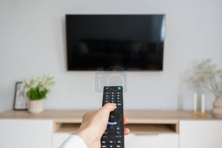 female hand hold tv remote control and press button to turn on television, sitting on couch in living room at cozy apartment, entertainment and relax at home