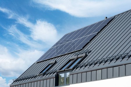 Foto de Conceptos de fuentes de energía renovables, verdes o alternativas. Paneles solares fotovoltaicos sobre un techo de la casa sobre fondo azul del cielo. Azotea con tejas de metal y tragaluz ventanas - Imagen libre de derechos