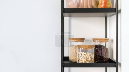 stockage des produits alimentaires et des gruaux dans des récipients en verre sur un support en métal noir dans une pièce avec mur blanc, concept zéro déchet, espace organisé à l'intérieur