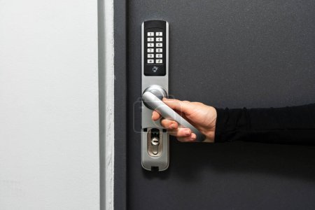 Close up view of woman hand push the doorhandle down, opened the apartment. Self check-in at hotel room or rented house. Security lock at the office door with password code on the smart digital keypad