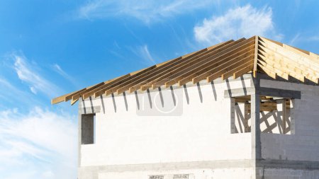 Téléchargez les photos : Vue du bâtiment inachevé depuis les blocs de béton et le toit avec des planches de treillis en bois à l'extérieur sur fond bleu ciel - en image libre de droit