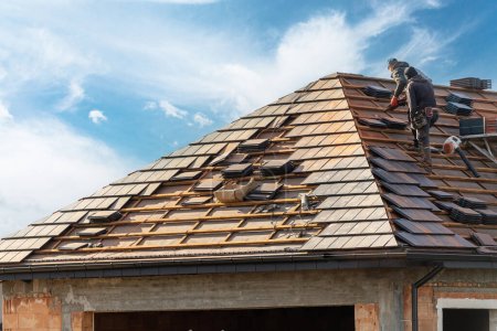  proceso de construcción, los trabajadores del tejado instalar baldosas de metal gris en la parte superior del techo con marco de madera al aire libre en el fondo del cielo azul 