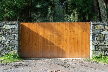 Photo for Wide and wooden automatic sliding gates with remote control installed in high stone fence wall. Concept of security and protection on private property - Royalty Free Image